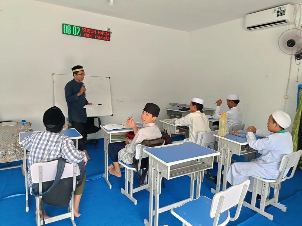 Kegiatan belajar di kelas SMP dengan meja biru dan papan tulis